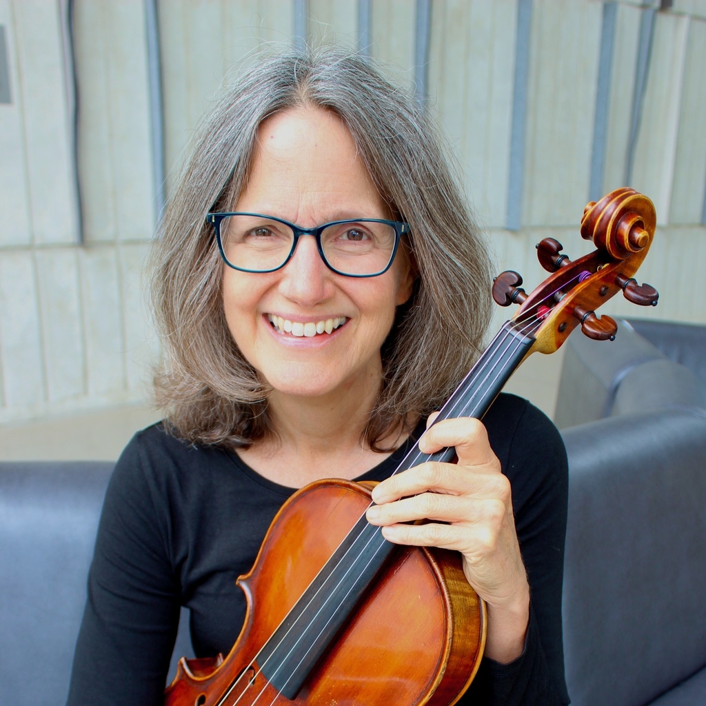 Elizabeth Oakes, seated on a leather couch in Voxman Music Building and holding her viola